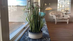 Una habitación con un ventanal grande, una planta en maceta, una silla de mimbre y una lámpara.