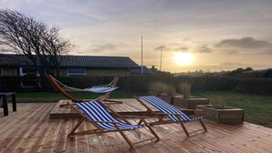 Una terraza de madera con dos sillones reclinables a rayas y una hamaca.