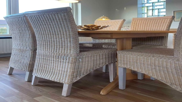 Comedor con sillas de mimbre y una mesa de madera, con iluminación colgante y vistas al exterior a través de una ventana.