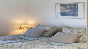 Una cama bien hecha con ropa de cama y almohadas estampadas, una lámpara de noche y un cuadro en la pared.