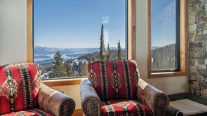 Quarto com duas poltronas de couro voltadas para uma grande janela com vista panorâmica de montanhas e árvores.