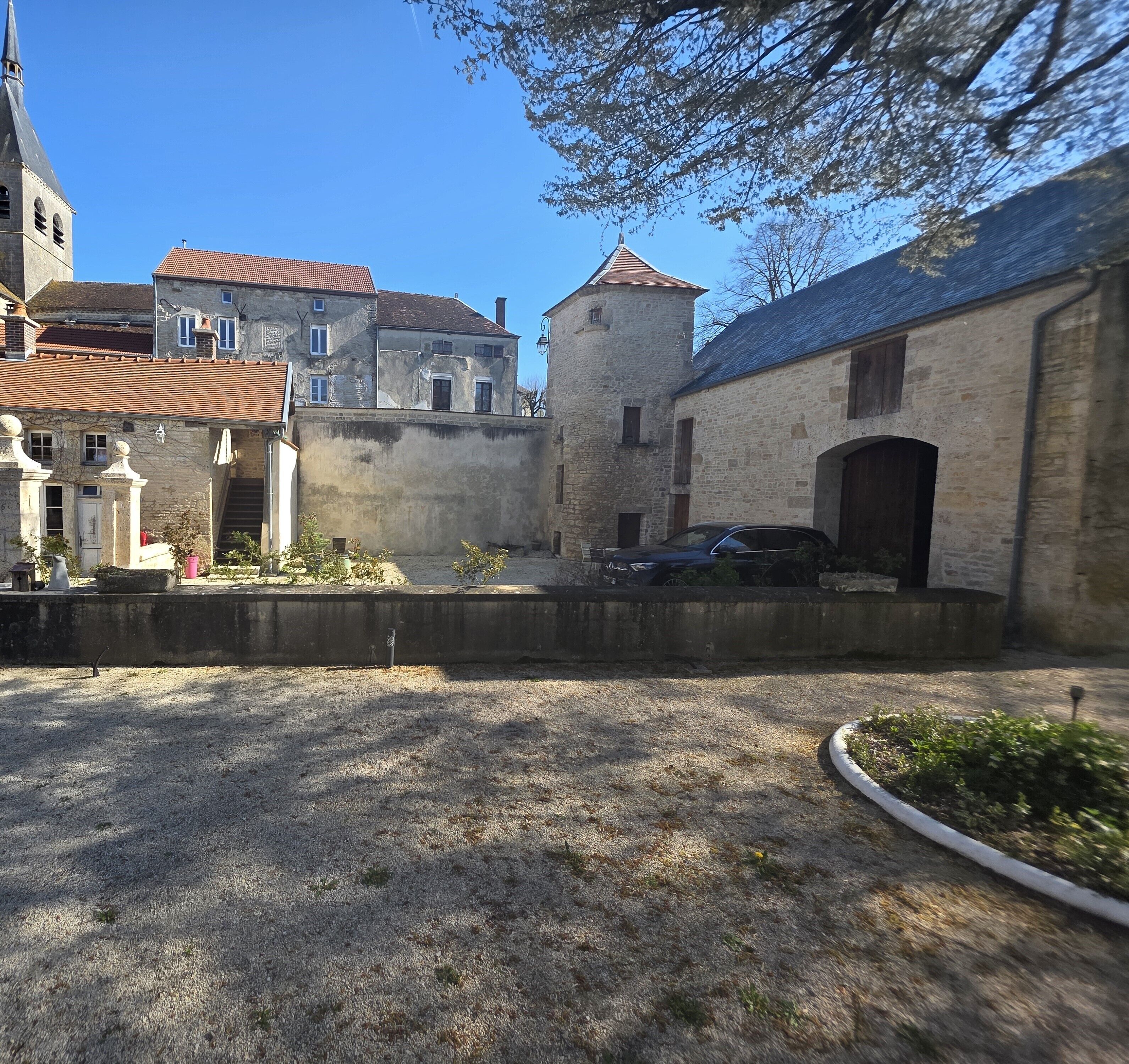 A courtyard with stone buildings, a tower, and a car parked in front.