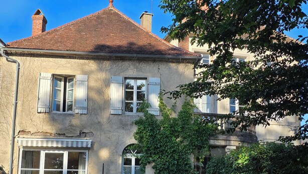 A two-story house with a brick roof, white shutters, and a garden with outdoor furniture.