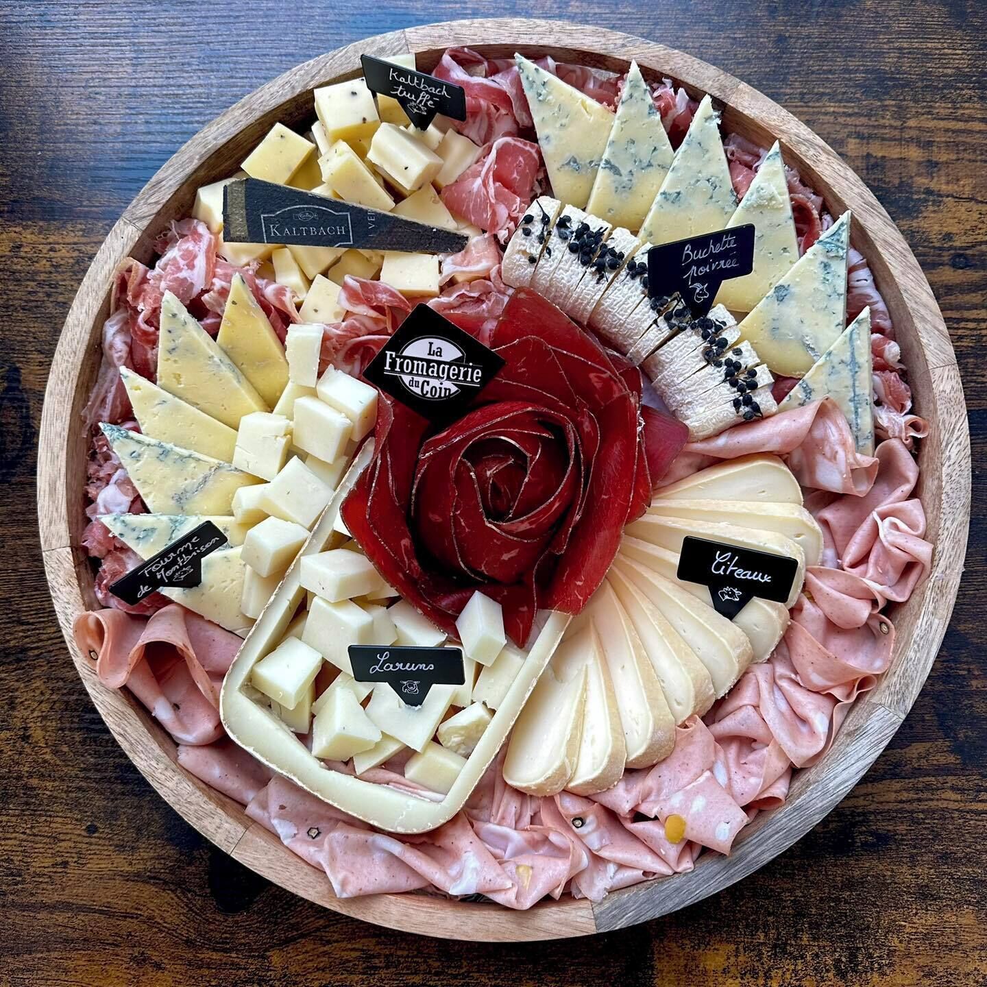 Una tabla de embutidos con varios quesos, carnes y una decoración central de rosas.