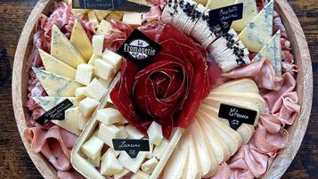 Una tabla de embutidos con varios quesos, carnes y una decoración central de rosas.