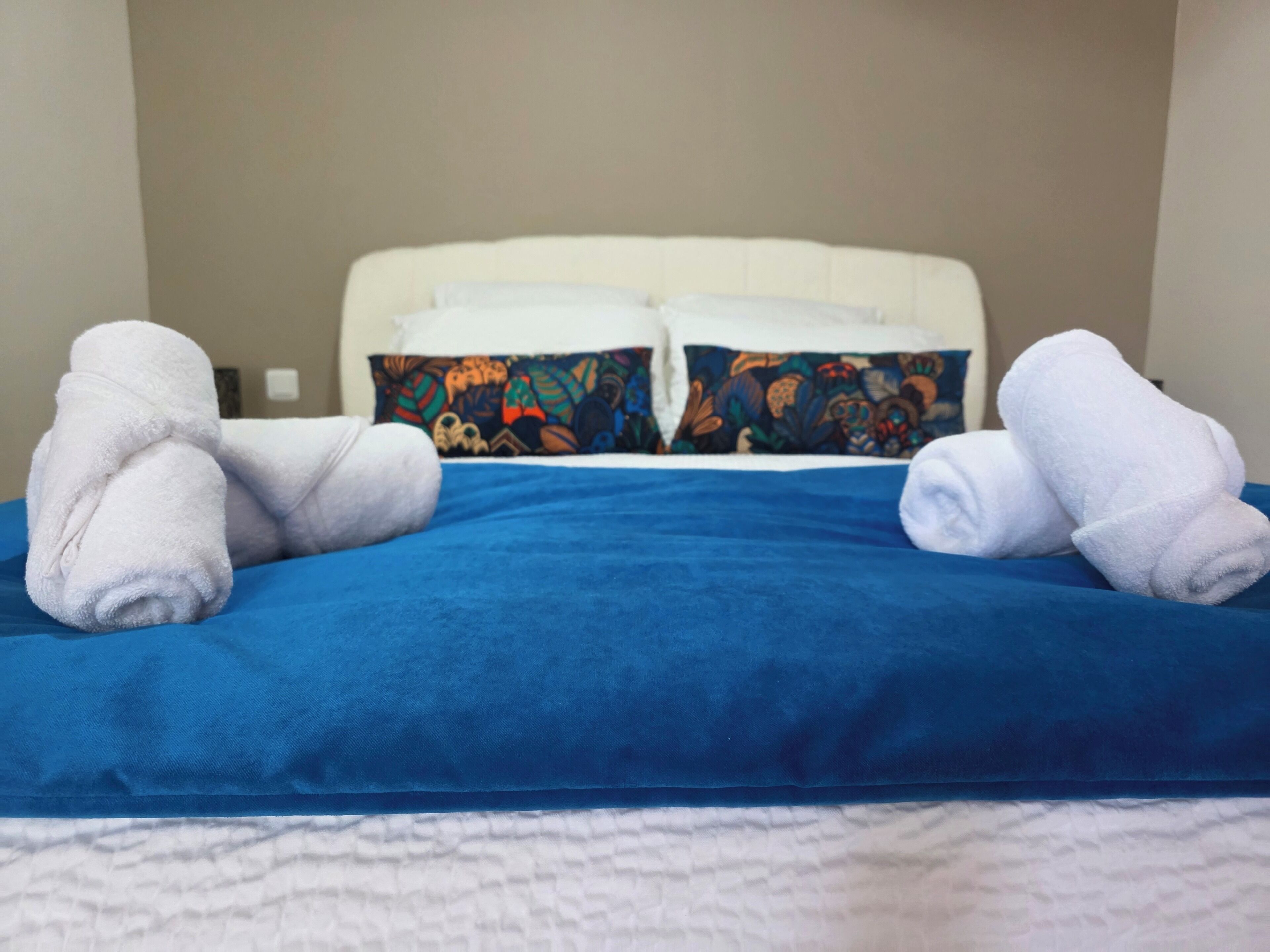 A bed with blue bedding and white pillows, two white towels folded on the bed.