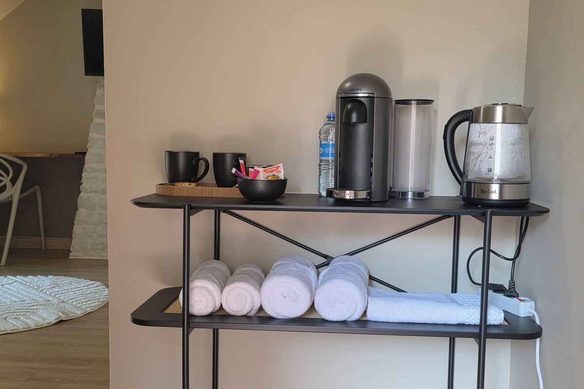 Una kitchenette con cafetera, hervidor y un estante con toallas dobladas.