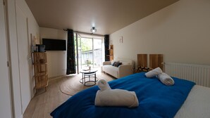 A hotel room with a bed, a sofa, a television, a small table, and a window with curtains.