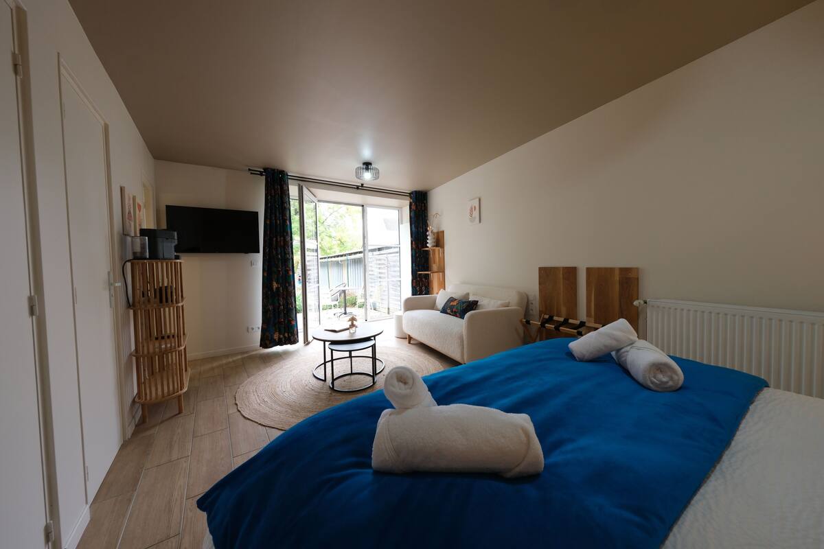 Una habitación de hotel con cama, sofá, televisor, una mesita y ventana con cortinas.
