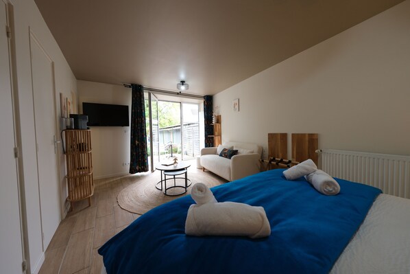 Una habitación de hotel con cama, sofá, televisor, una mesita y ventana con cortinas.