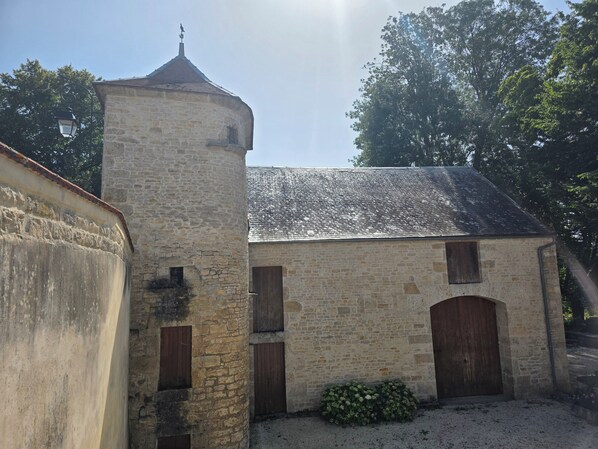 A stone building with a tower, wooden doors, and a small garden area. - Manoir de l'Échauguette (Laignes)