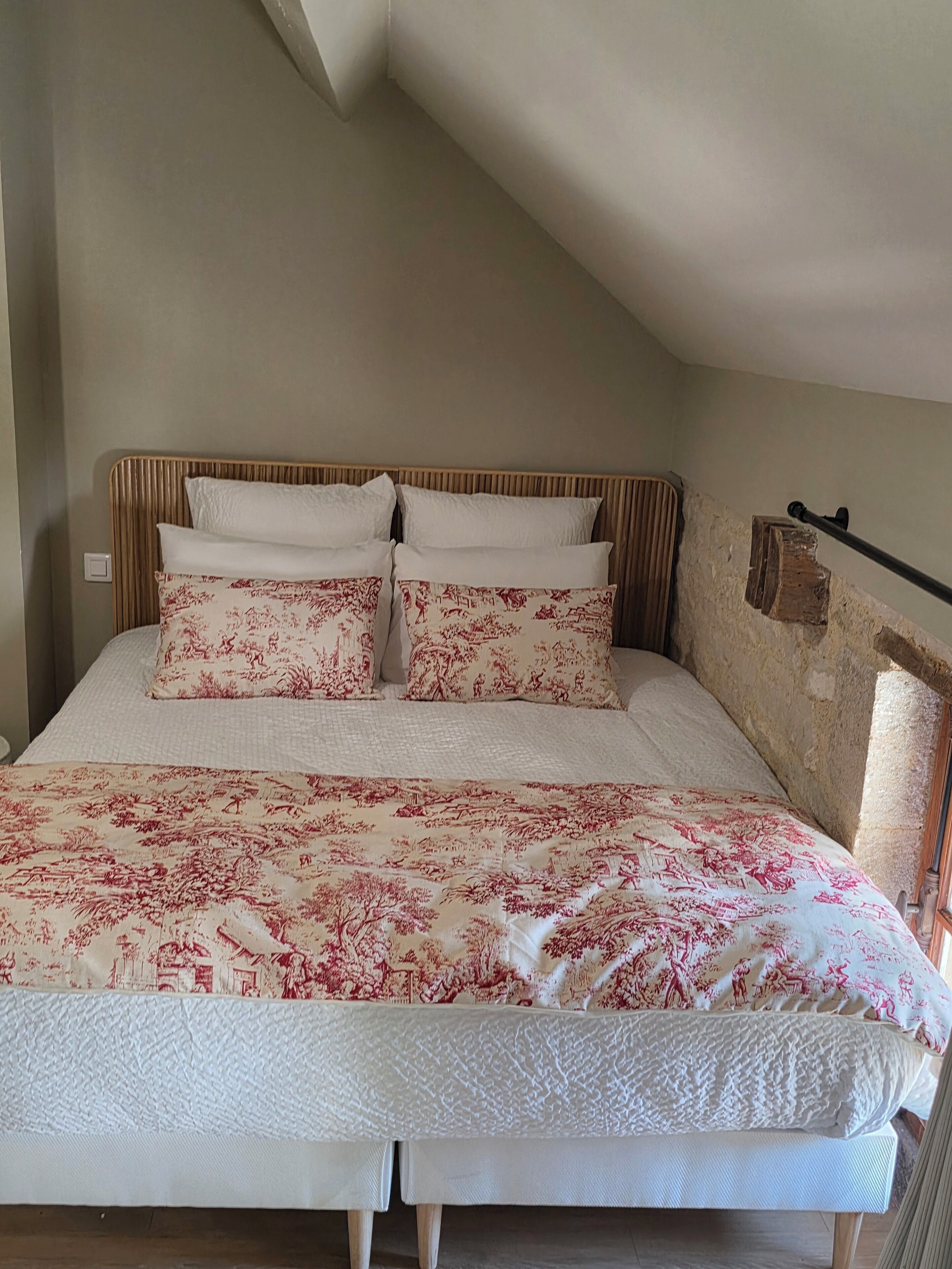 A bedroom with a sloped ceiling, a bed with floral bedding, and a wooden headboard.