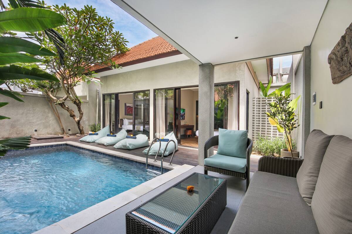 A modern outdoor pool area with a glass table, lounge chairs, and a sofa.