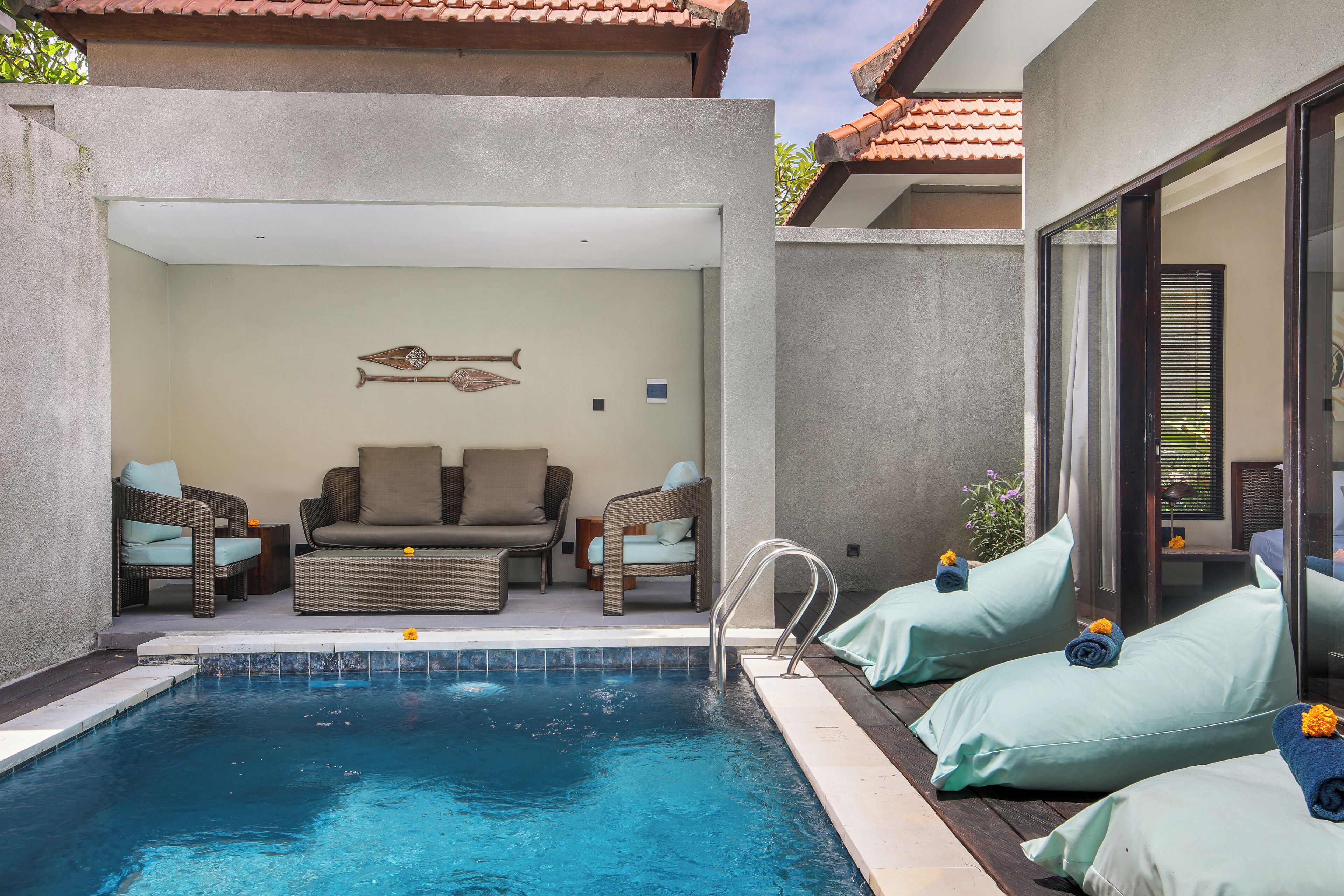 Un espace piscine extérieur moderne, comprenant des chaises longues et un ensemble de canapés, une petite table et un élément décoratif mural représentant des poissons.