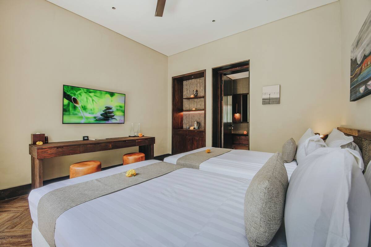A hotel room with two beds, a wooden desk, a television, and a painting on the wall.