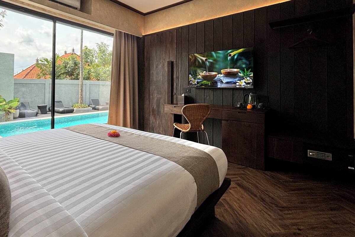 A hotel room with a large bed, a TV, a small table, and a view of a swimming pool.