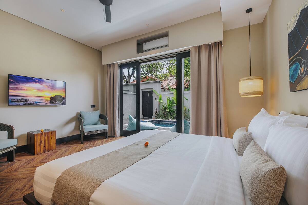 A hotel room with a large bed, a chair, a small table, and a view of a swimming pool.