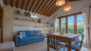 Ein gemütliches Zimmer mit einem blauen Sofa, einem Holzesstisch und Blick auf Grün hinter großen Fenstern.