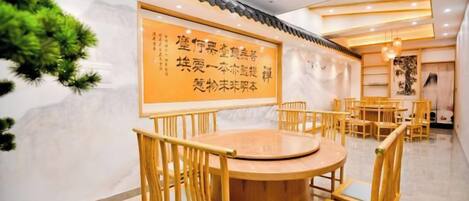 A dining area with round tables and chairs, a wall with a framed menu, and a ceiling with recessed lighting.