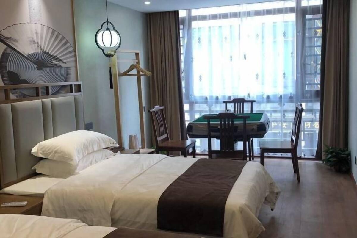 A hotel room with a large bed, a desk with a chair, and a view of the city through large windows.
