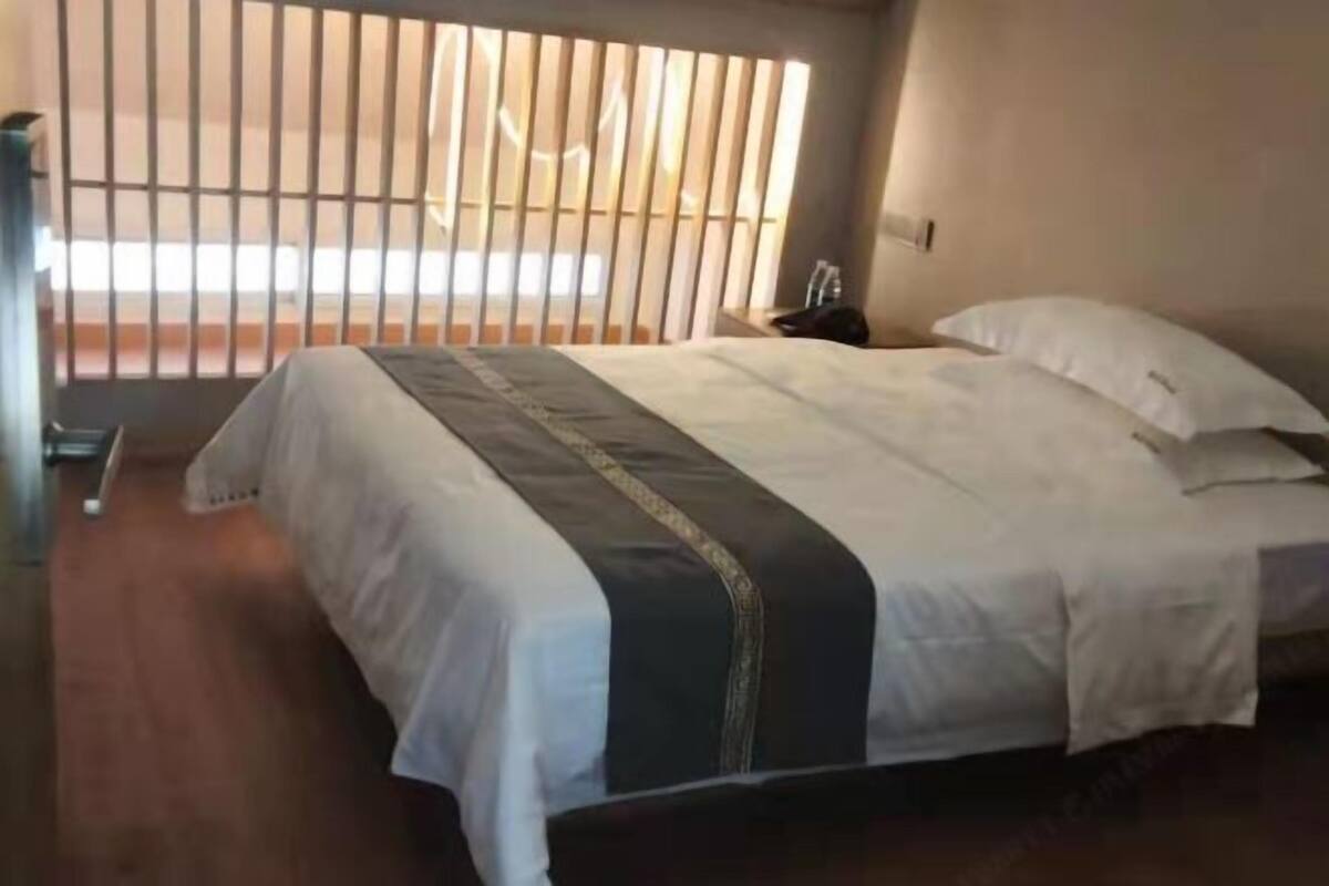 A hotel room with a bed, a nightstand, and a window with blinds.
