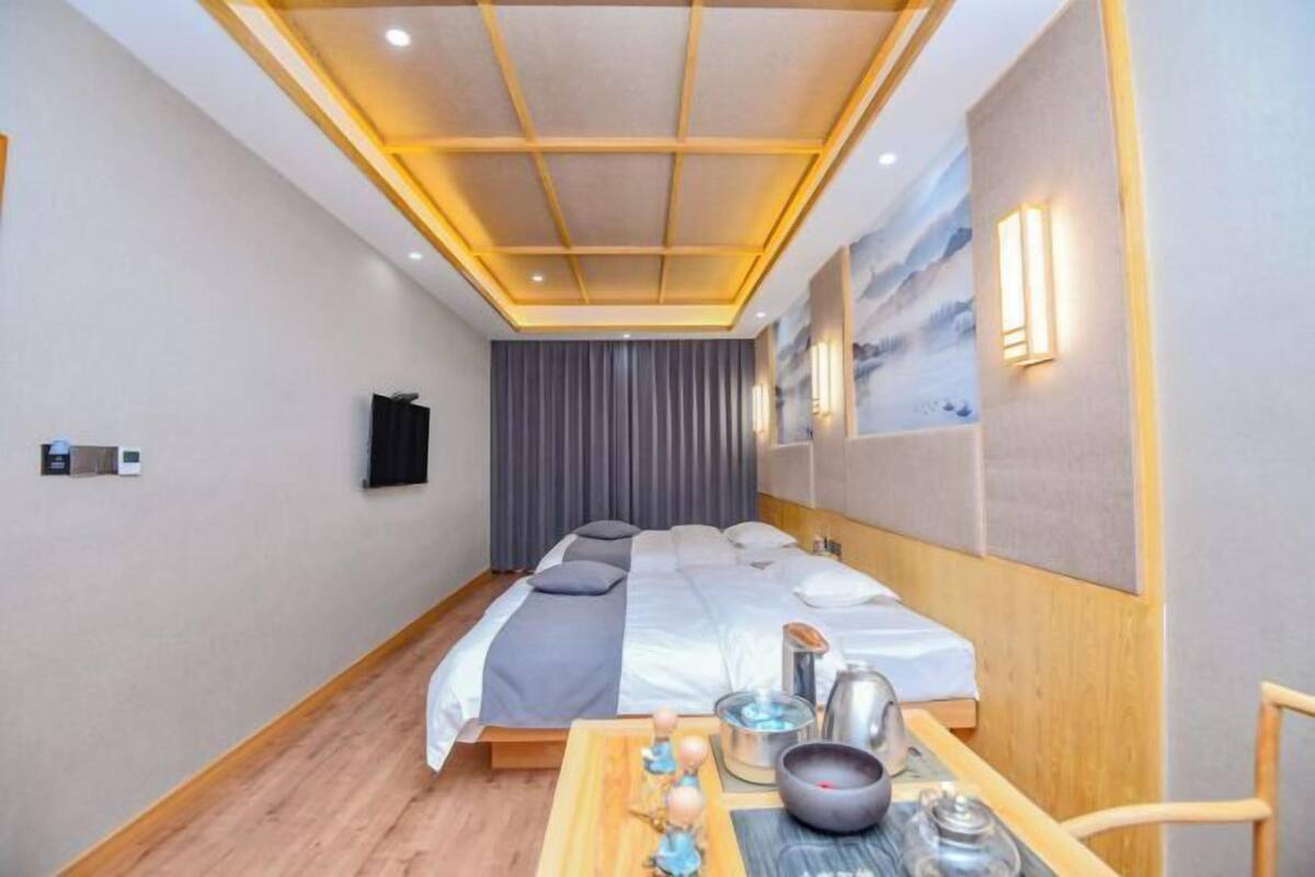 A hotel room with a bed, bedside table, wall-mounted lamp, and a painting.