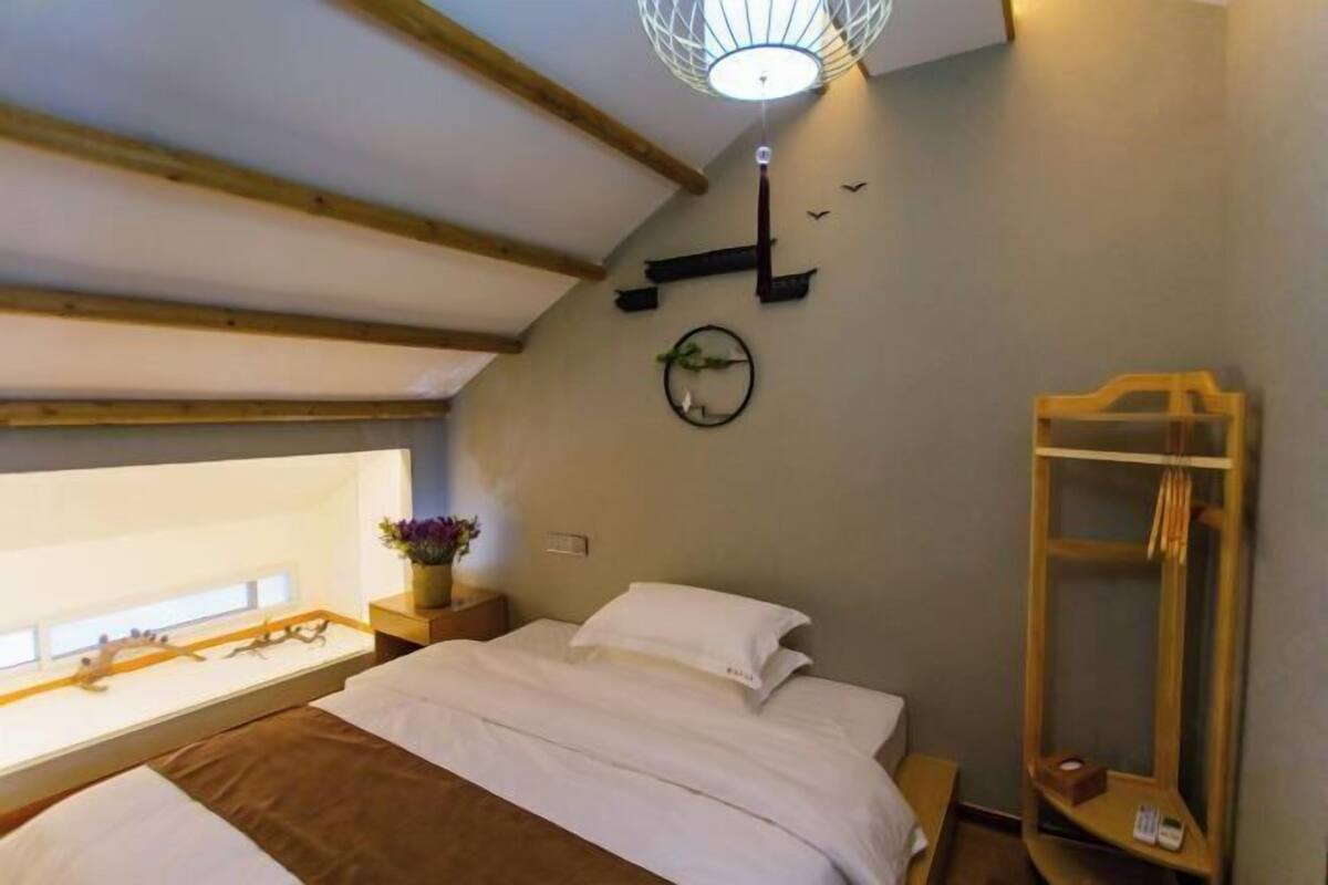 A bedroom with a bed, a bedside table with a lamp, a window, and a wooden shelf.