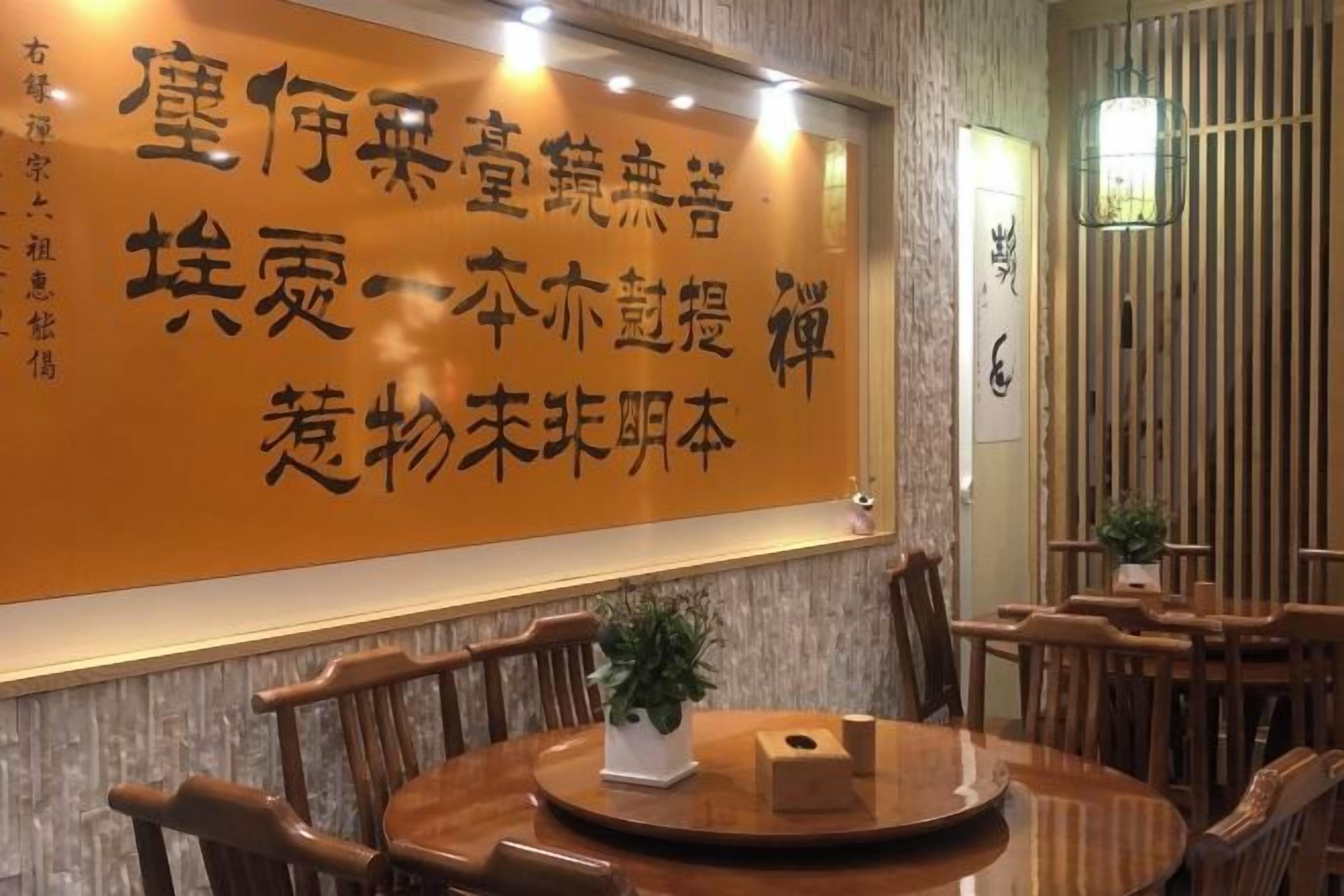 Een restaurantinterieur met een grote muur waarop Chinese karakters staan, houten meubels en een potplant.