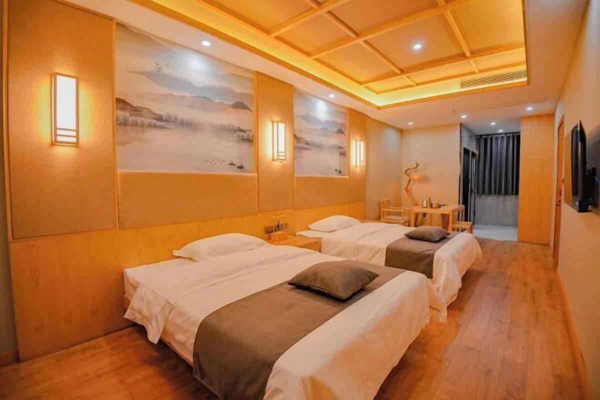 A hotel room with two beds, a desk, a chair, and a painting on the wall.