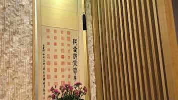 Ett traditionellt japanskt rum med en skjutdörr av trä, en vägg dekorerad med kalligrafi och en krukväxt med rosa blommor.