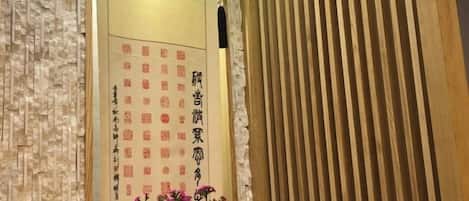 Habitación tradicional japonesa con puertas correderas de madera, un muro con caligrafía y una planta en maceta con flores rosadas.