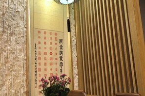 Habitación tradicional japonesa con puertas correderas de madera, un muro con caligrafía y una planta en maceta con flores rosadas.