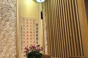 Habitación tradicional japonesa con puertas correderas de madera, un muro con caligrafía y una planta en maceta con flores rosadas.