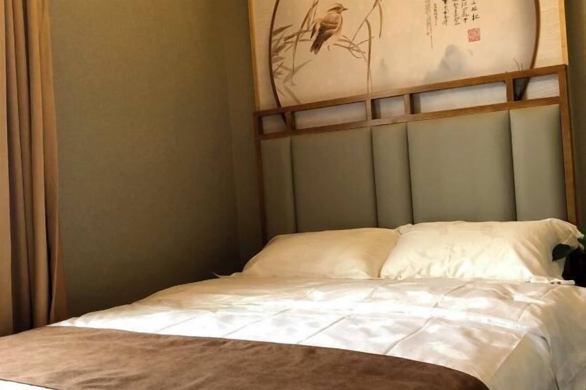 A neatly made bed with a headboard, a wall with a decorative panel, and a curtain.