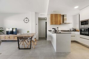 Una cocina moderna con una isla central, electrodomésticos integrados y un comedor con mesa y sillas de madera.