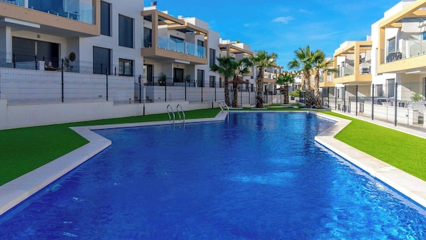 Un moderno edificio residencial con piscina, balcones y palmeras.
