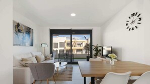Una sala moderna con sofá, mesa de centro y mesa de comedor con sillas. Hay un ventanal con vistas a edificios.