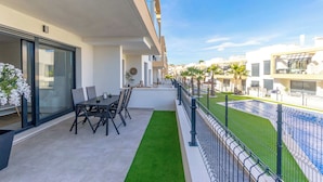 Un balcón con una mesa y sillas, un pequeño jardín y una piscina.
