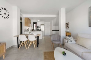 Una sala moderna con un sofá, un comedor con sillas, una cocina con armarios y electrodomésticos, y un reloj de pared.