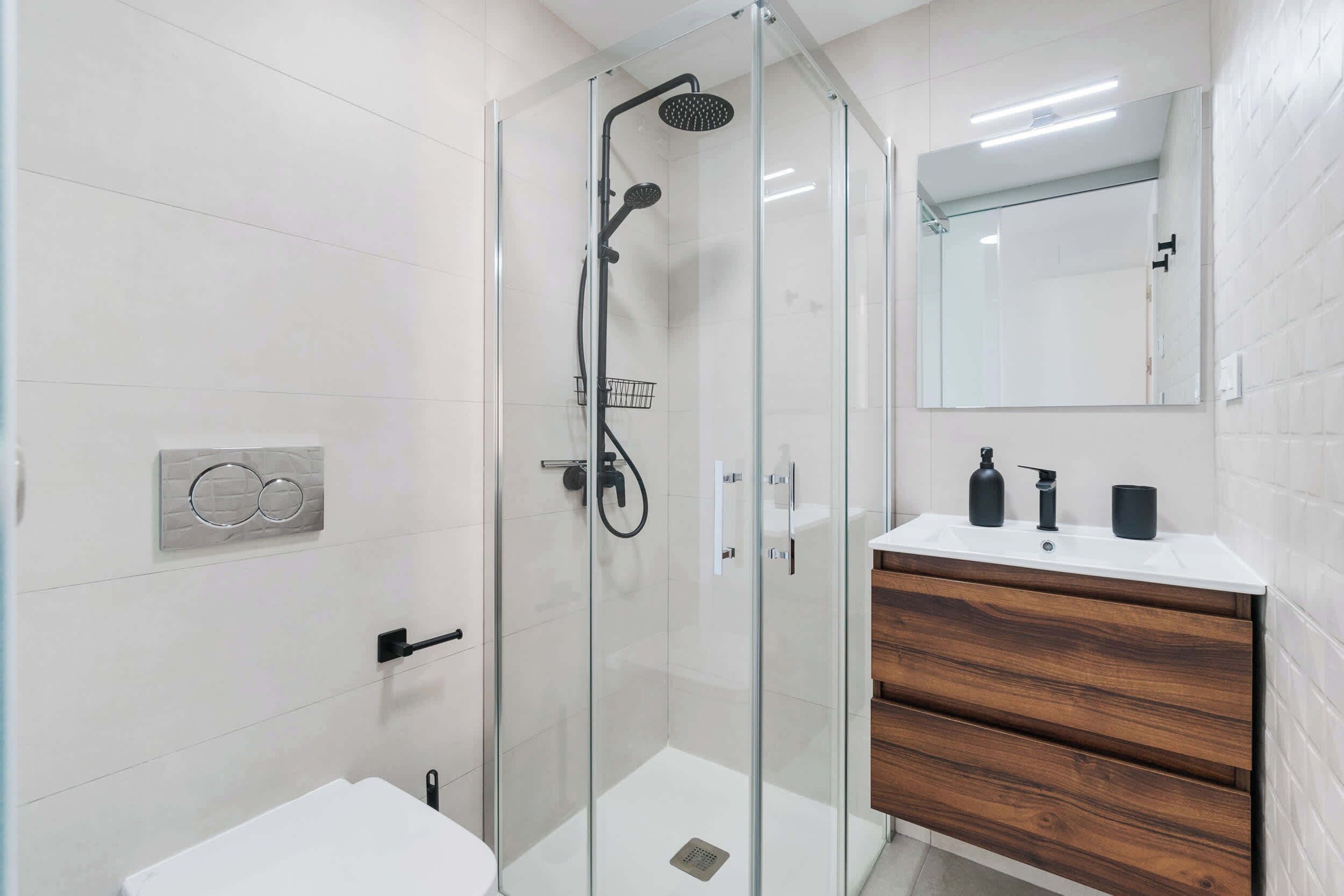 Un baño moderno con ducha de vidrio, inodoro blanco y tocador de madera con espejo.