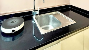 Una cocina con encimera negra, pileta de acero inoxidable y un armario blanco con puertas de vidrio.