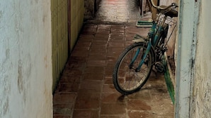 Un estrecho pasillo con suelo de baldosas, una bicicleta apoyada en una pared y una motocicleta estacionada a lo lejos.