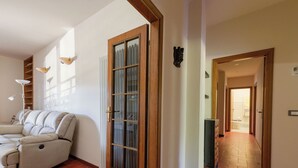 Un saló amb un sofà, una porta de fusta amb panells de vidre, un radiador i un passadís que condueix a una altra habitació.