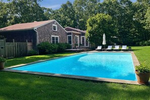 A rectangular swimming pool with a wooden deck and lounge chairs, surrounded by a well-maintained lawn and a wooden fence.