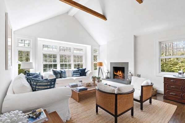 A spacious living room with a fireplace, white furniture, and large windows.