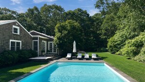 Une piscine résidentielle à l’eau d’un bleu limpide, entourée d’une pelouse bien entretenue et d’arbres.