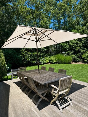 Una terraza de madera al aire libre con una mesa y sillas, rodeada de abundante vegetación.