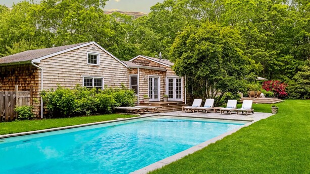 Un jardin avec une piscine, deux maisons en bois et une pelouse verdoyante.