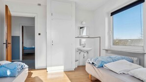 A modern bedroom with two beds, a window, a bathroom with a sink, and a door leading to another room.