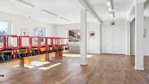 A spacious room with a long wooden bench, white walls, and a door marked with an exit sign.